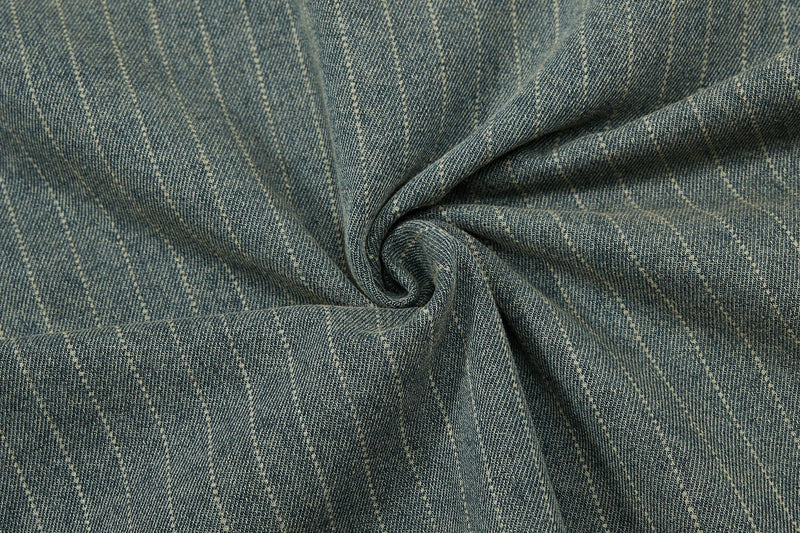 Close-up of vintage pinstripe denim fabric with a textured, washed blue-gray weave and soft folded swirl detail