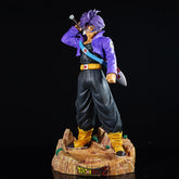 The Seakoff Trunks Collectible Figure – Dragon Ball Z, measuring 50cm, depicts the iconic character in a sword pose with interchangeable heads. Dressed in a purple jacket, black pants, and yellow boots, Trunks stands confidently on a rocky base with one hand on his head.