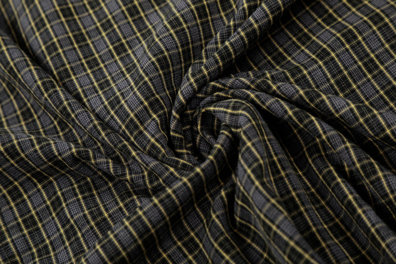 Close-up of black and gray distressed plaid shirt fabric with yellow grid pattern and raw-textured folds