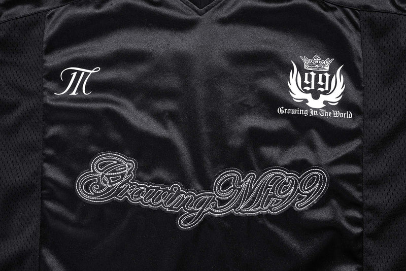 Front chest close-up of black jersey with PI logo, crest graphic, and Growing In The World text