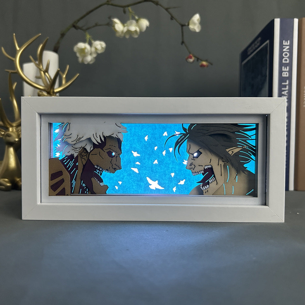 The Attack on Titan brand Anime Light Box features Eren vs Zeke with intense expressions and a dynamic color-changing effect, set against a bright blue background with white butterfly-like shapes, all framed elegantly in white. In the backdrop, blurred are a deer figurine and book.