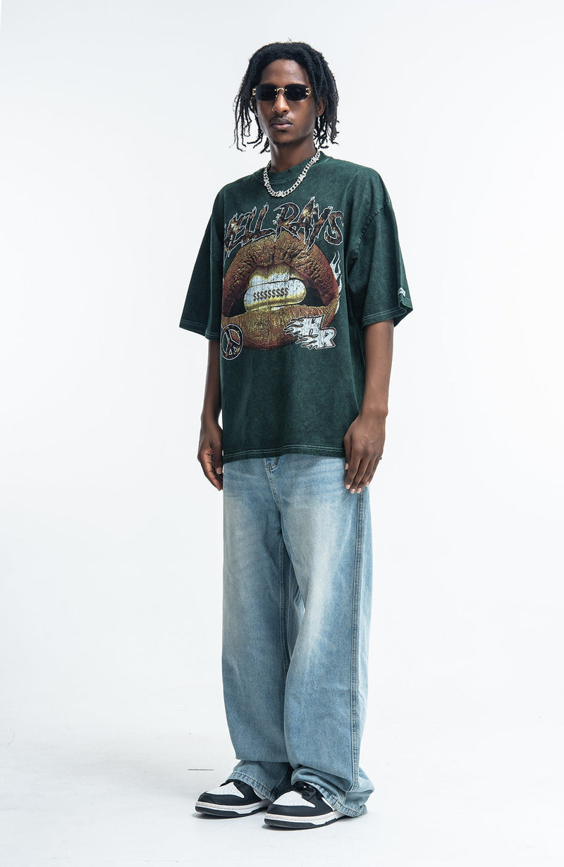 Model wearing a vintage washed dark green Hellrays graphic tee with oversized light blue jeans and black sneakers on a white background