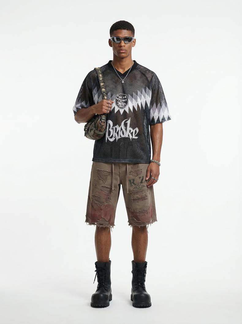 Model wearing a black mesh streetwear soccer jersey with graphic print, distressed shorts, boots, and sunglasses