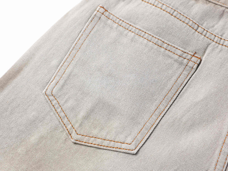Close-up of the back pocket on light gray washed denim pants with orange stitching