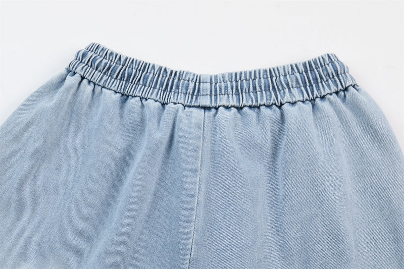 Close-up of light wash denim elastic waist and front seam, showing gathered waistband detail