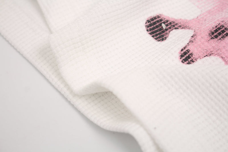 Close-up of white oversized graphic tee fabric with a faded pink skull print and black distressed details