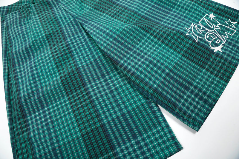 Green plaid shorts laid flat with white graphic on the leg