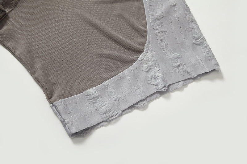 Close-up of a distressed mesh patchwork tee sleeve hem in taupe and light gray textured jersey fabric