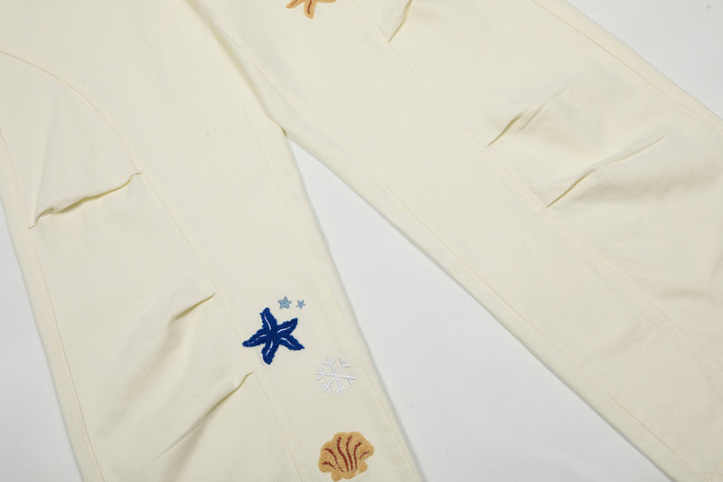 Close-up of cream cargo pants leg with embroidered star and snowflake motifs