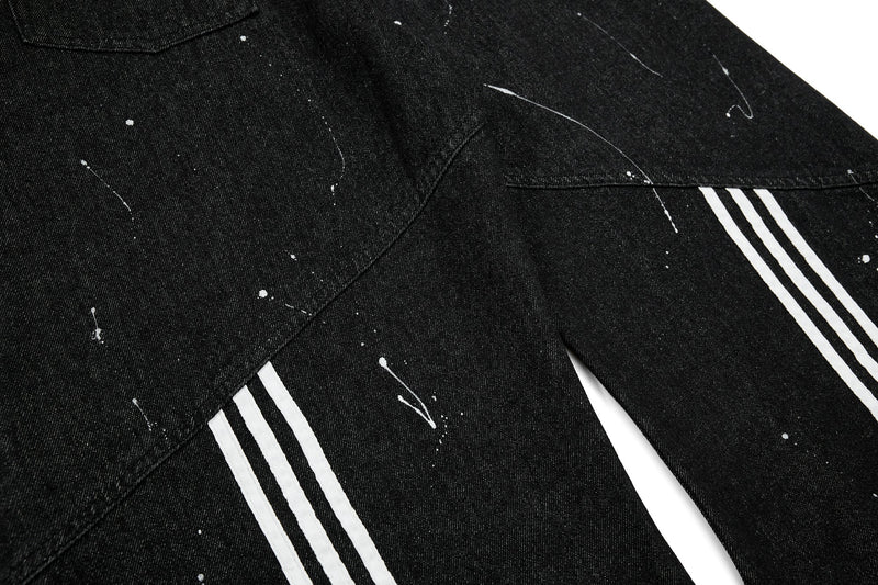 Black wide-leg jeans with white triple stripes and paint splatter, angled close-up
