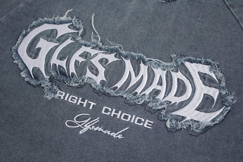Close-up of a faded gray graphic T-shirt with frayed patch lettering and vintage streetwear print