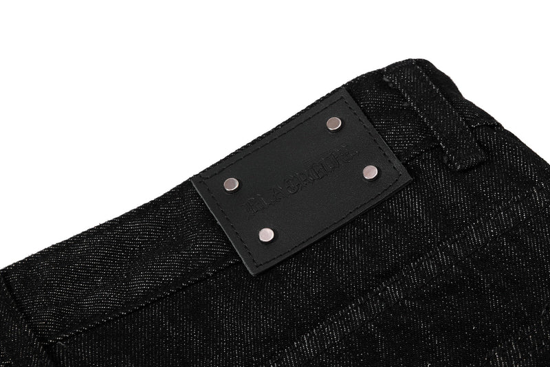 Close-up of black waistband patch with metal studs on denim pants