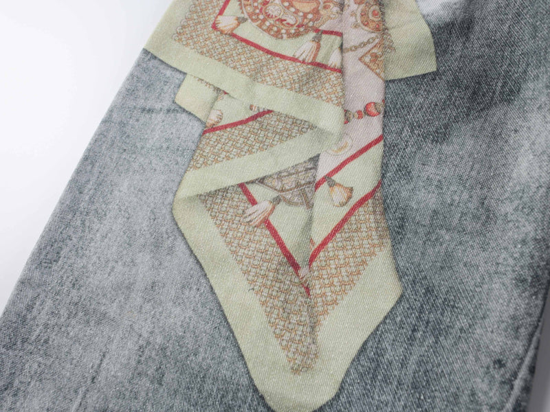 Close-up of front jeans panel with pale green tie graphic over faded denim