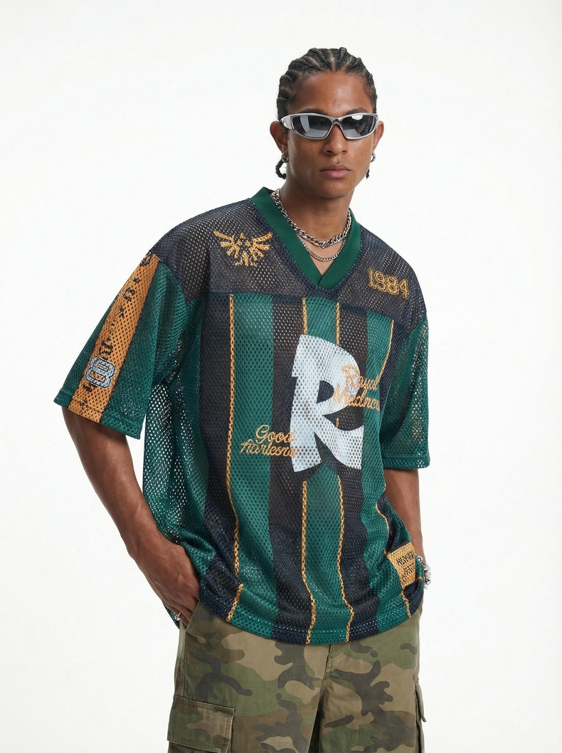 Man wearing sunglasses and braided hair, styled in a green mesh jersey T-shirt with black and gold stripe details and camo pants