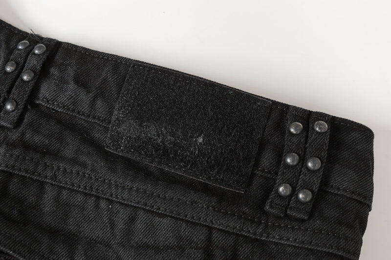 Close-up of black denim waistband with Velcro patch and metal stud accents