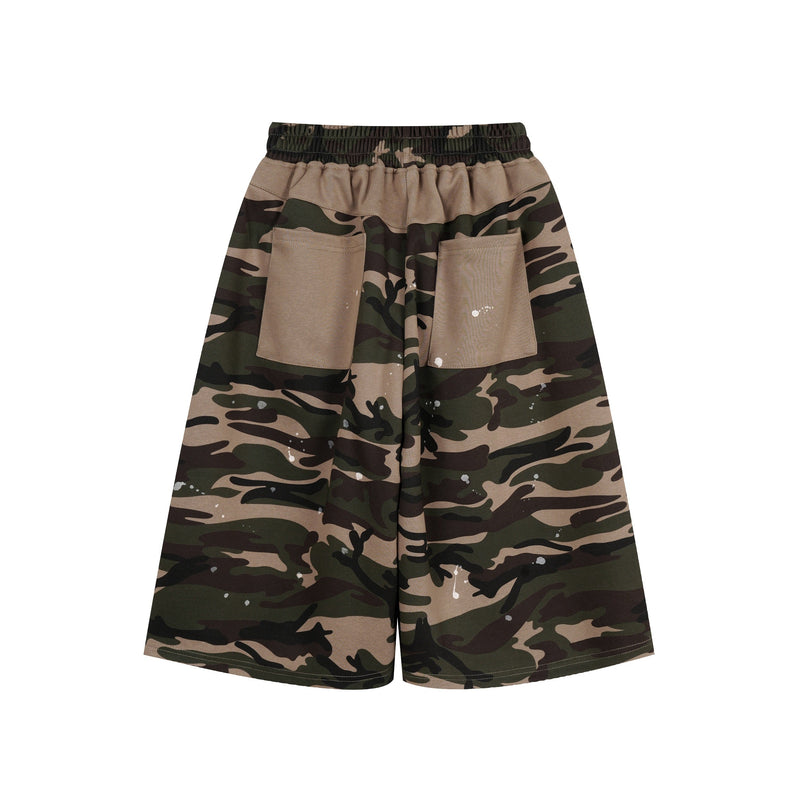 Back view of camo patchwork baggy shorts with tan patch pockets and white paint splatter
