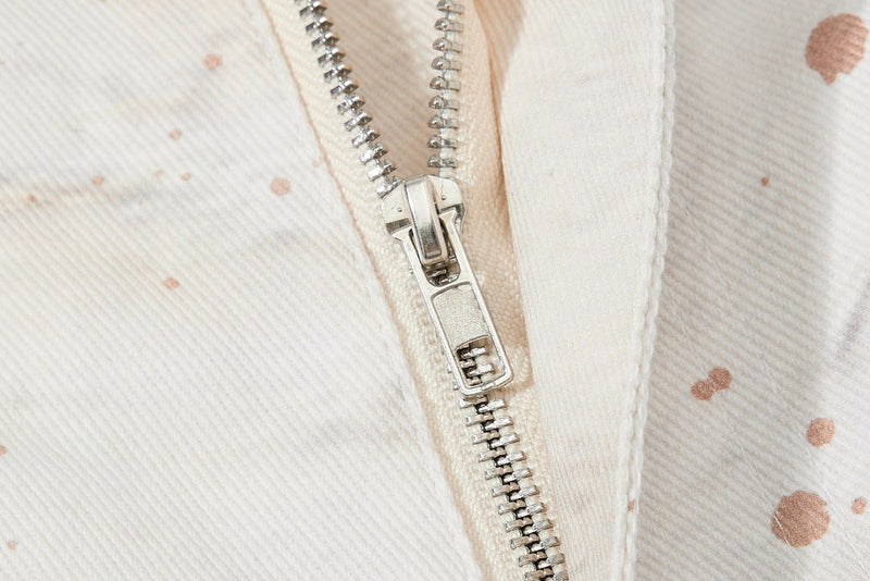 Close-up of the front zipper on cream denim jeans with splatter print