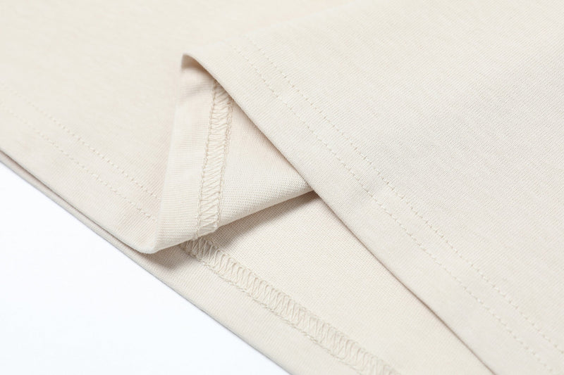 Close-up of cream oversized tee fabric with visible seams and hem stitching on a clean white background