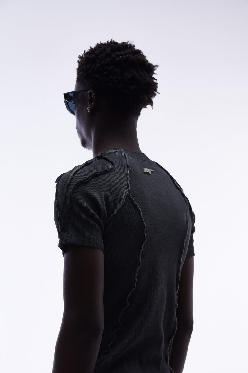 Black raw seam compression tee with deconstructed stitching, worn by model from the back in a minimalist studio shot