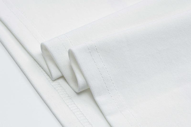 Folded white graphic tee with visible stitched hem and soft cotton texture, shown in a clean product close-up