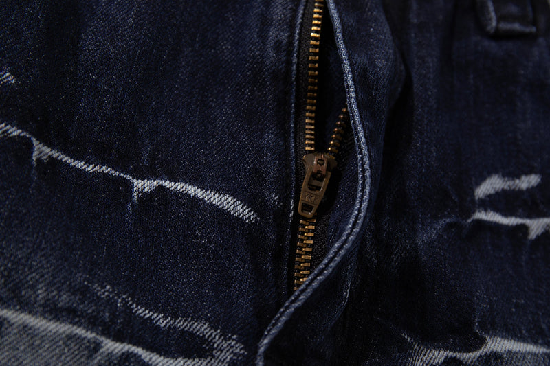 Close-up of the front fly on deep indigo jeans with brass zipper and cracked-wash denim