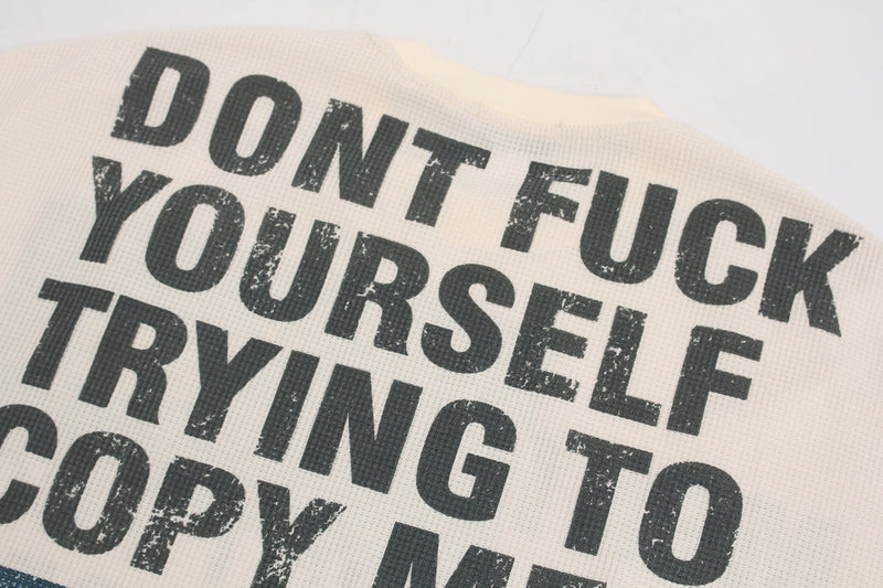 Close-up of distressed black slogan print on cream waffle fabric
