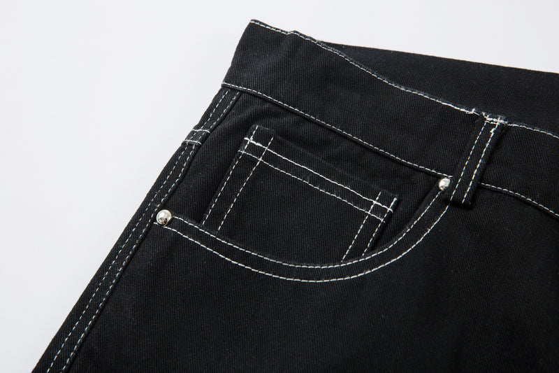 Close-up of black jeans front pocket with white stitching and metal rivet