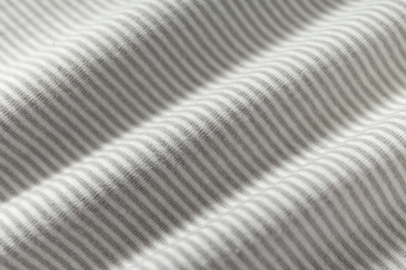 Close-up of light gray striped knit fabric with soft textured waves on a relaxed fit raglan T-shirt