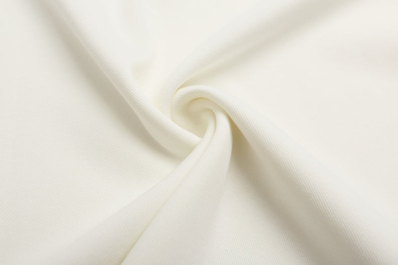 Cream-colored fabric close-up with soft twisted folds, showing the texture of a studded collar graphic polo shirt