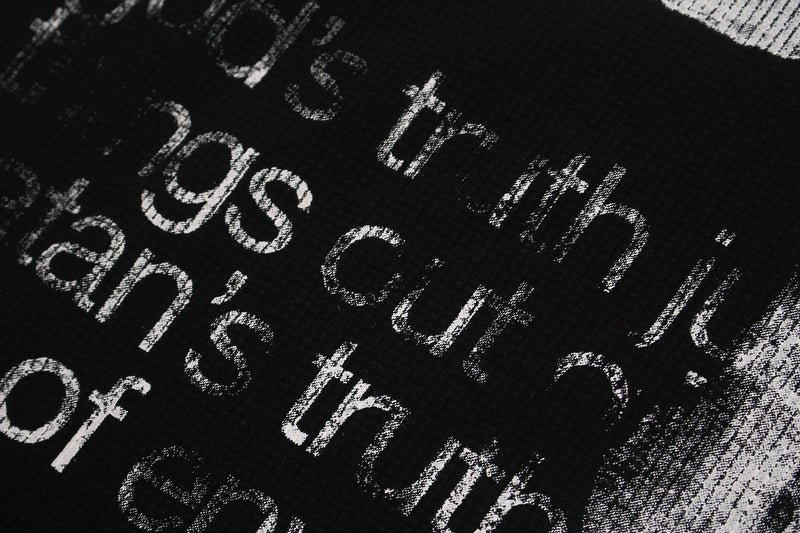 Close-up of black oversized graphic tee with distressed white gothic lettering and cross motif for streetwear style