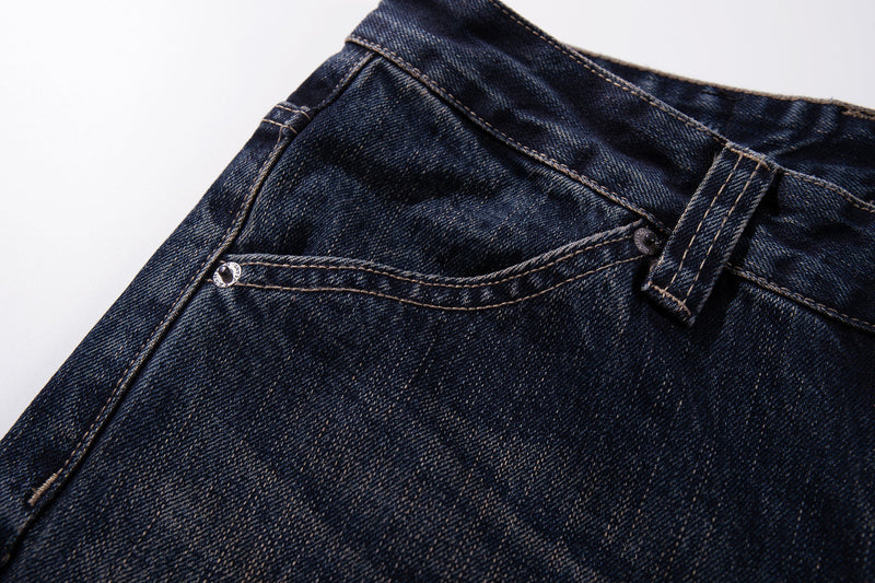 Close-up of the front waist pocket on dark wash denim with topstitching and rivets