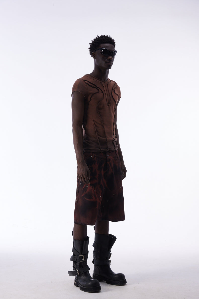Model wearing a brown sculpted panel cotton tee with raw seams, paired with dark shorts and black buckle boots on a white background