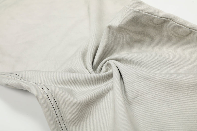 Close-up of light gray denim fabric with contrast stitching and gathered fold detail