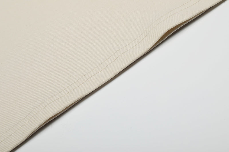 Close-up of a cream oversized cotton T-shirt hem with visible stitched seam and soft ribbed fabric texture