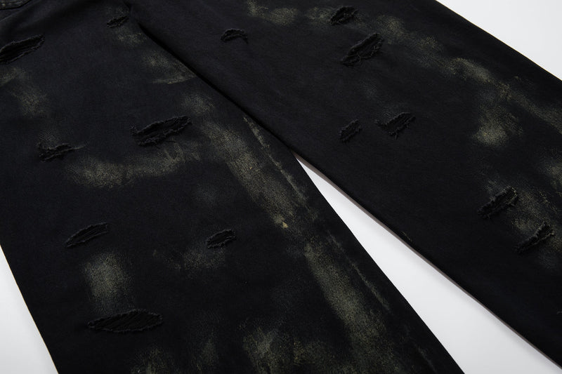 Close-up of black wide-leg jeans leg with scattered ripped details and faded wash
