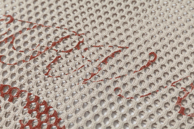 Close-up of cream mesh football jersey fabric with red distressed graphic details, retro oversized streetwear style