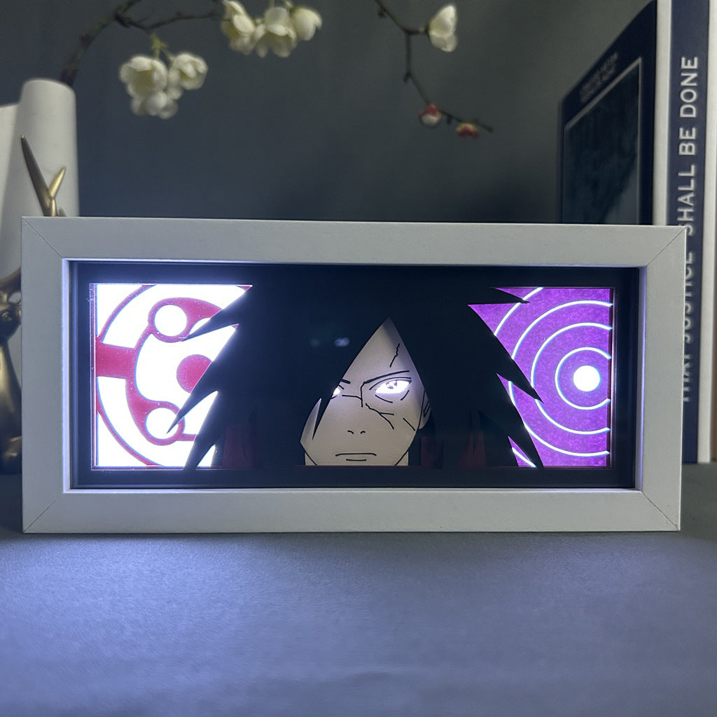 The Naruto Anime Light Box features a 3D LED lamp of Madara Uchiha with long black hair and a serious expression. It has dynamic color-changing effects, including red, white, and purple concentric circles, all within a sleek white frame.