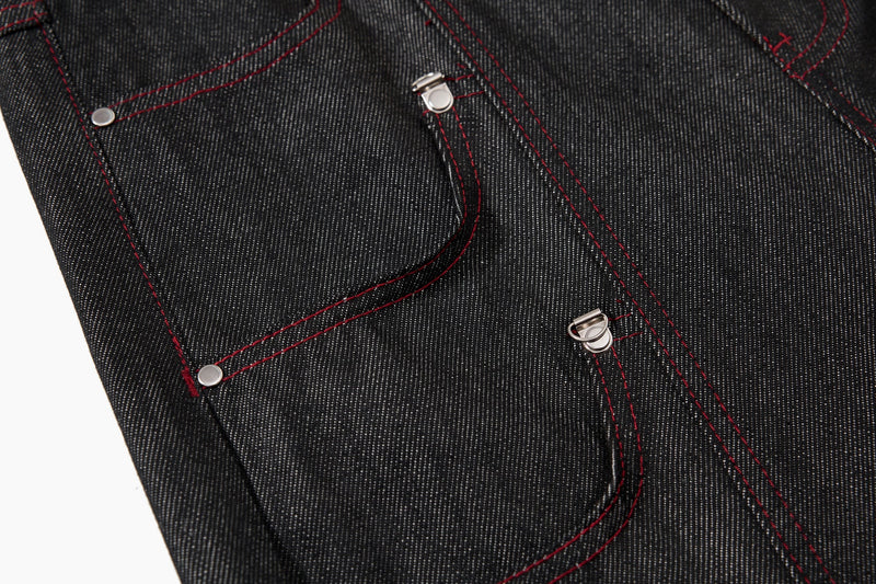 Close-up of black denim side pocket panels with red contrast stitching and silver rivets