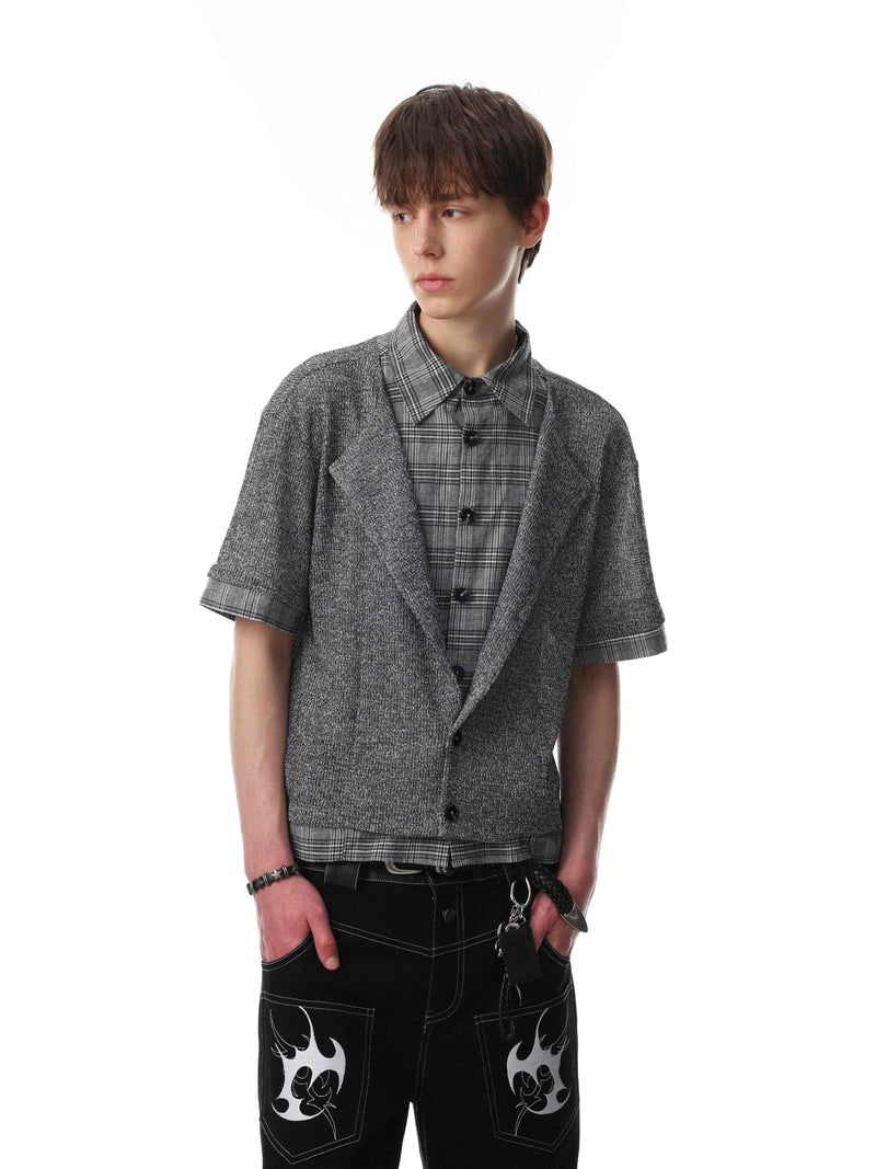 Model wearing a layered gray knit check shirt with short sleeves over a plaid button-up and black streetwear pants