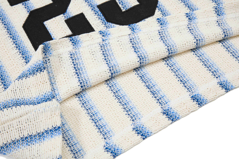Close-up of cream knit tee with blue varsity stripes and black collegiate lettering, showing textured streetwear fabric