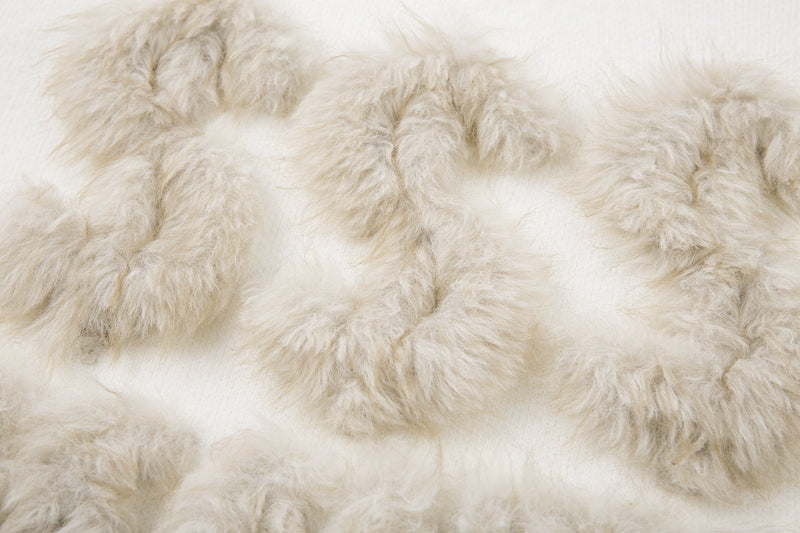 Close-up of cream faux-fur lettering on white knit sweater
