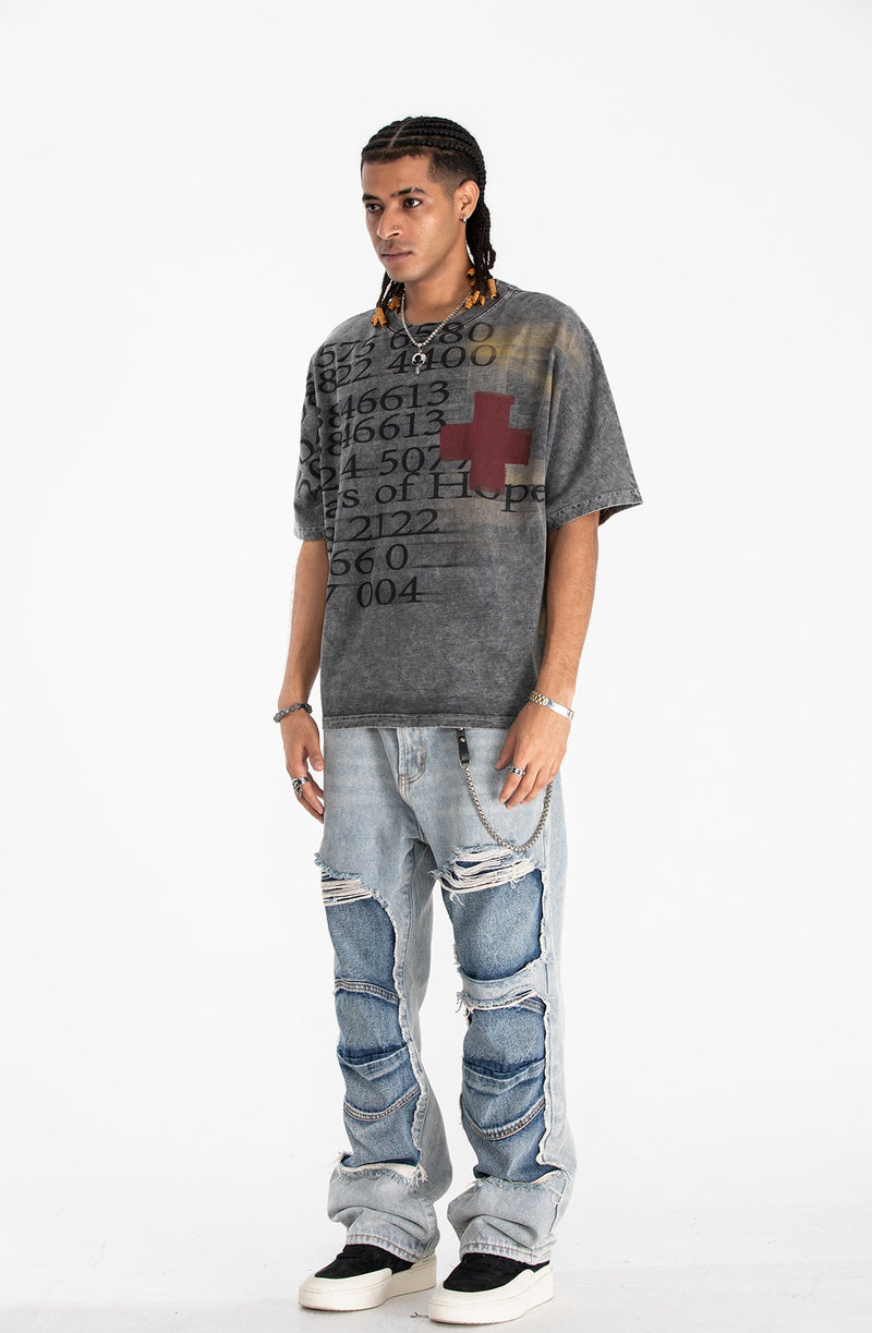 Model wearing a vintage wash oversized graphic tee with red cross print and distressed patchwork jeans on a white background