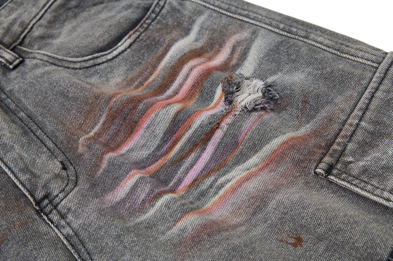 Close-up of gray cargo jeans with pink and white paint streaks and a frayed hole