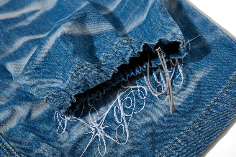 Close-up of elastic cuff and drawstring hem with embroidered graphic on denim