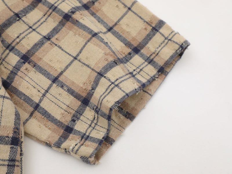 Close-up of beige and navy distressed plaid shirt sleeve with frayed hem and raw-edge streetwear styling