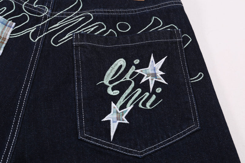 Close-up of back patch pocket on dark denim shorts with script embroidery and star patches