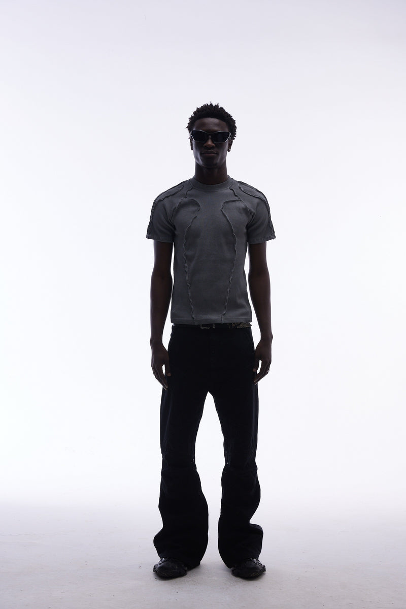 Model wearing a charcoal raw seam compression tee with deconstructed details, black pants, and sunglasses on a white background