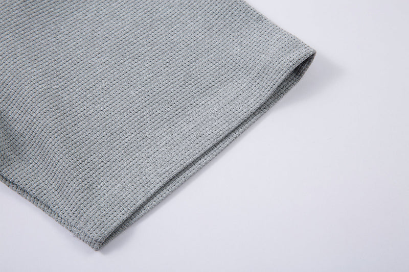 Close-up of a light gray textured half-zip neck graphic t-shirt sleeve folded on a white background