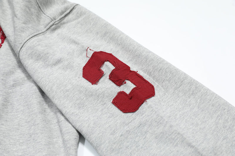 Close-up of red patch on light gray hoodie sleeve with stitched number design