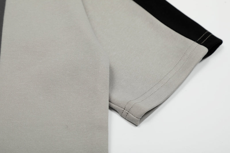 Close-up of a beige cotton tee sleeve with black contrast panel and visible stitched hem on a clean white background